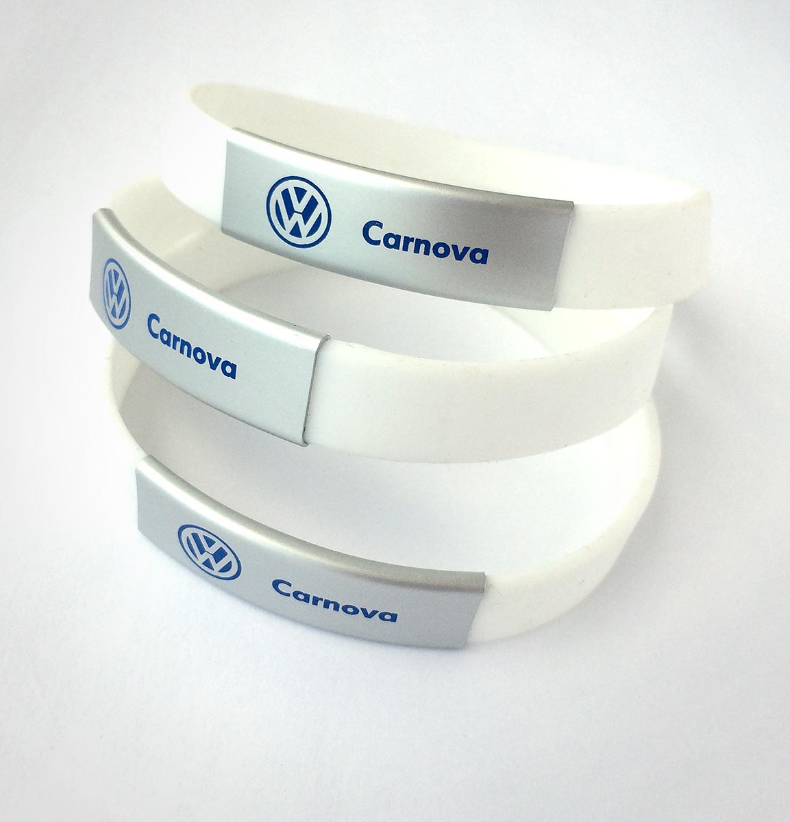 Reklamní bílé silikonové náramky s kovovou destičkou a potiskem loga Volkswagen Carnova