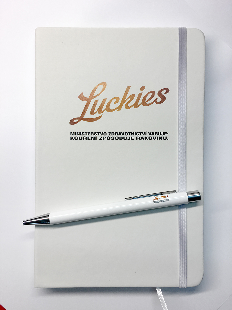 Bílý zápisník s gumičkou a kovové kuličkové pero s potiskem značky Luckies