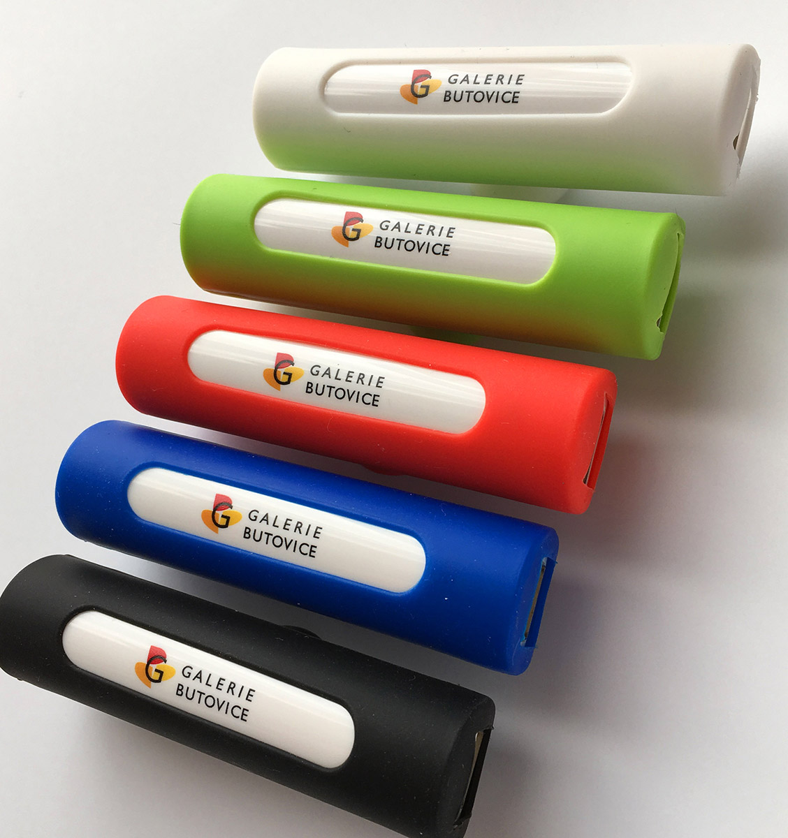 Pět barevných válcových powerbank s potiskem loga Galerie Butovice