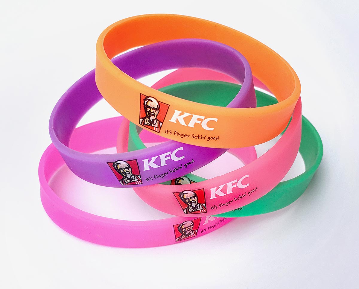 Reklamní silikonové náramky v oranžové, fialové a růžové barvě s potiskem loga KFC