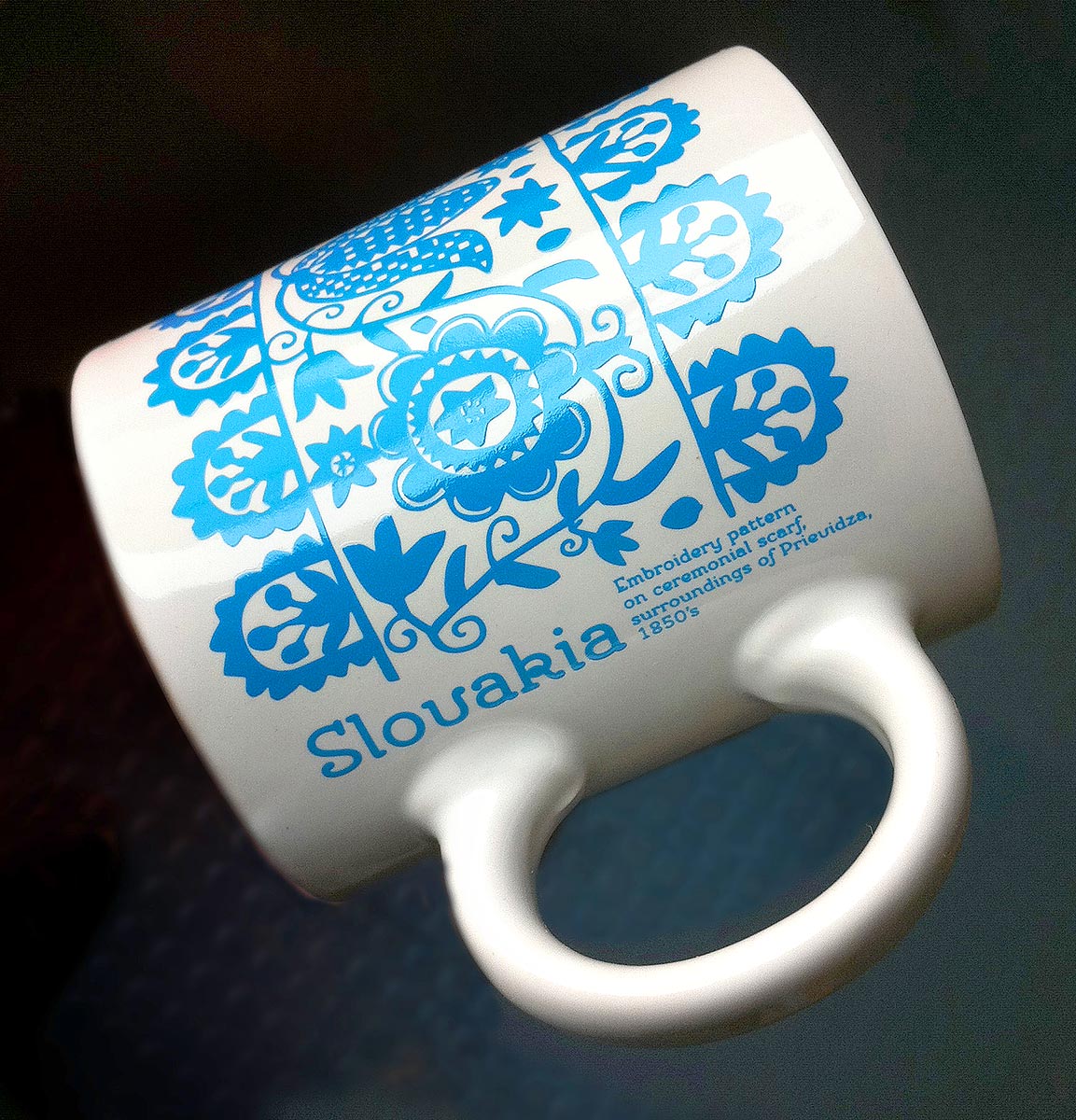 Reklamní bílý keramický hrnek s modrým folklorním vzorem a nápisem Slovakia